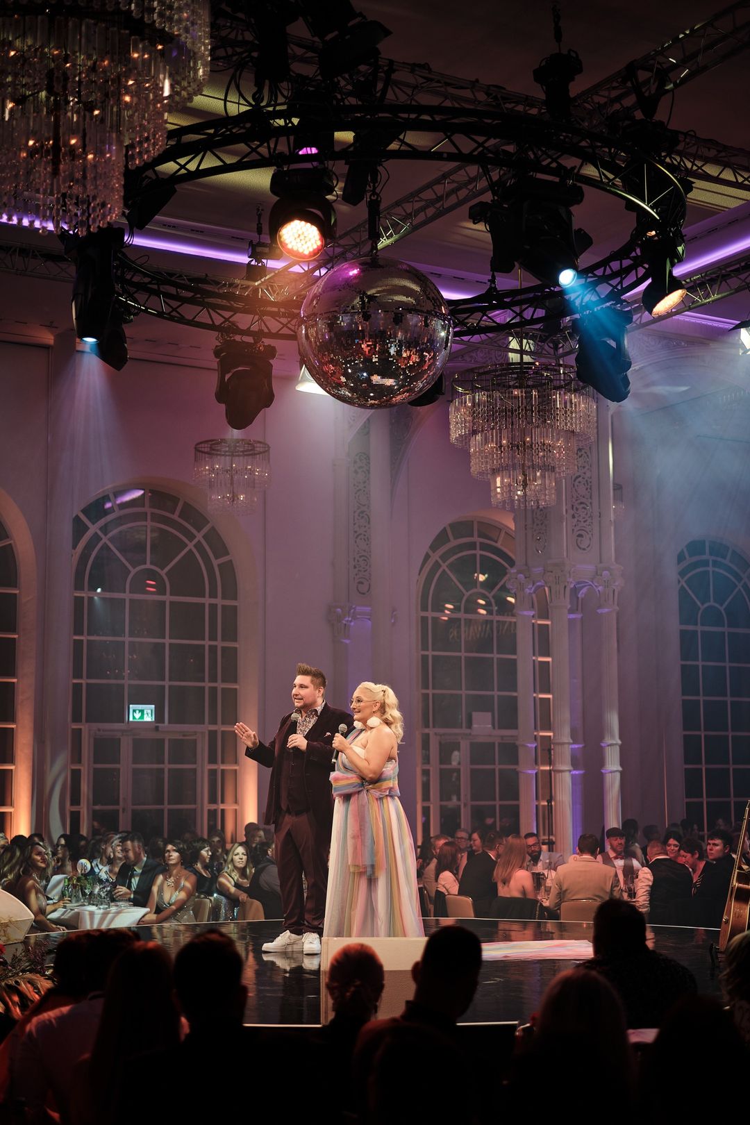 Benny Schmidt und Beatrix Schmiedel auf der Bühne der Flora Köln, über ihnen eine große Discokugel